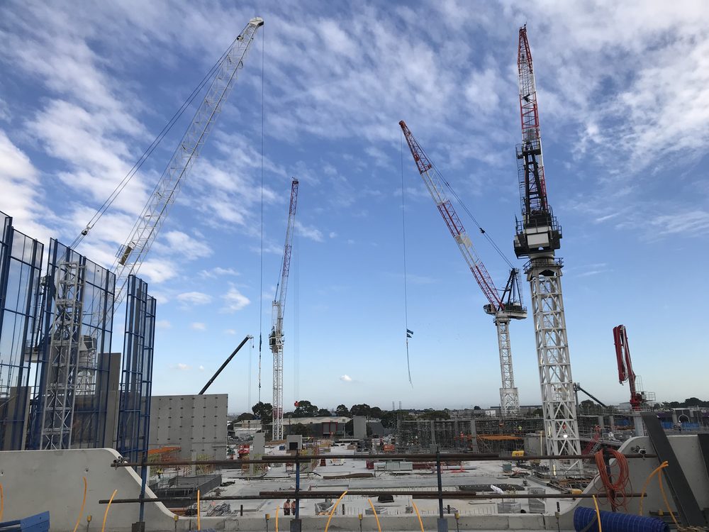 Multi-storey commercial construction site with tower cranes against a blue sky