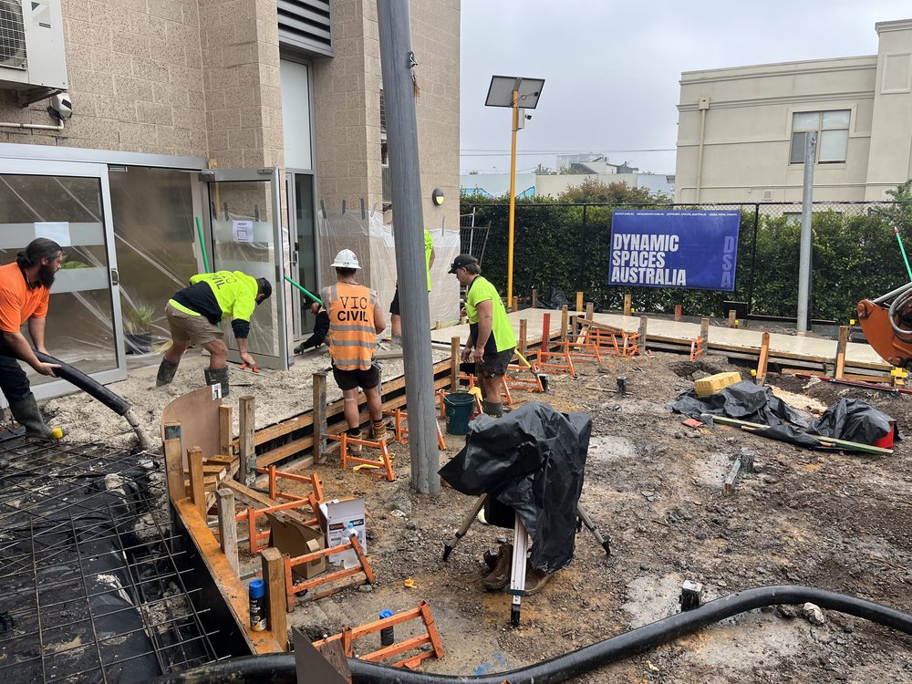 Workers forming and preparing concrete steps beside a commercial building