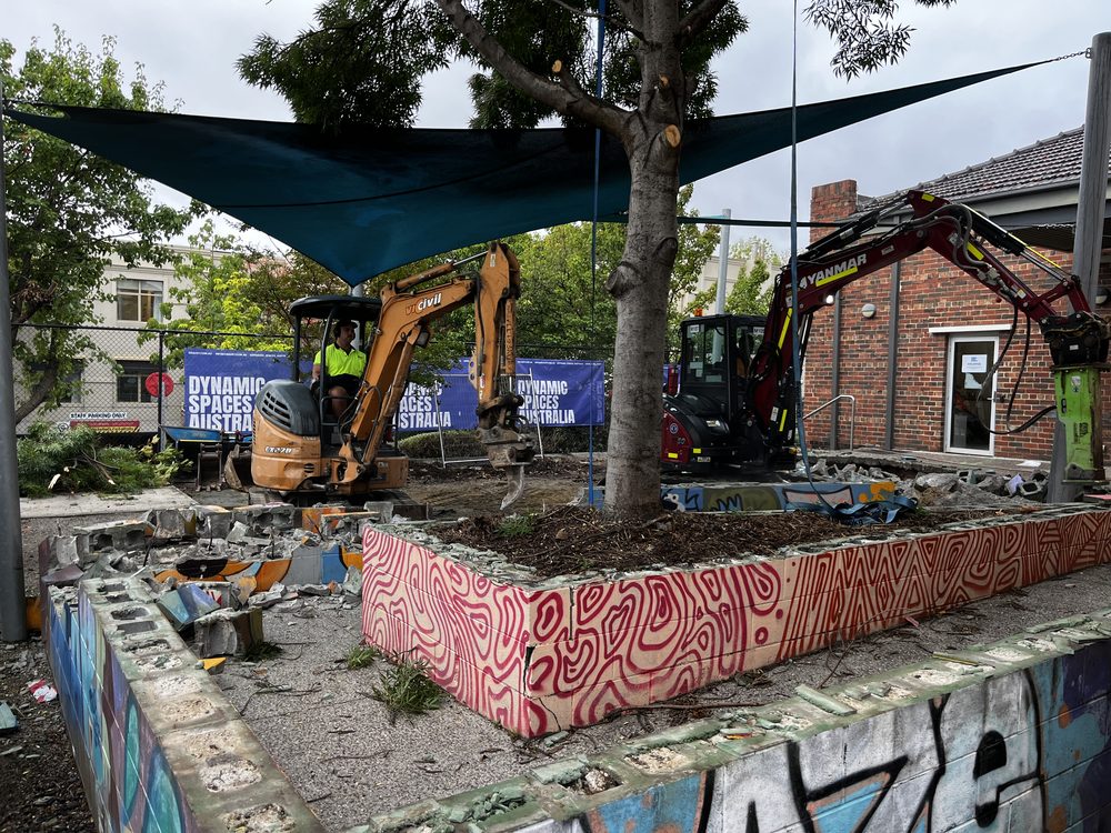 Excavator clearing a masonry stairway during demolition works, with DSA site banner behind