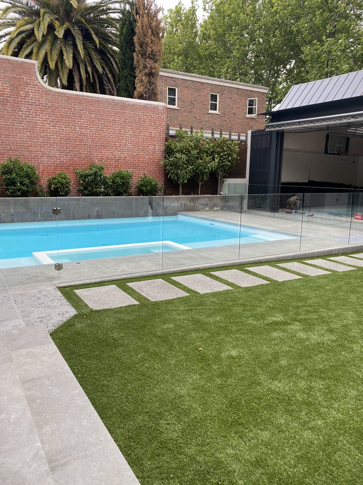 Pool with frameless glass fencing, a stepping-stone path and lawn in a landscaped backyard