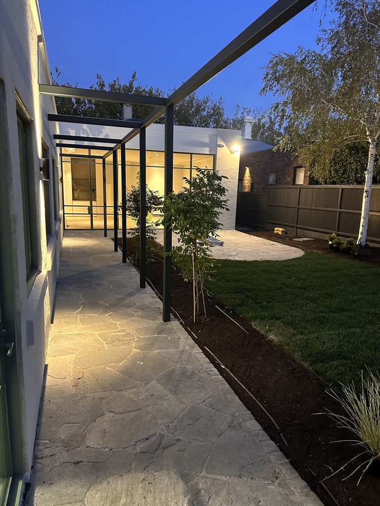 Stone paving path under a steel pergola beside a landscaped lawn at dusk