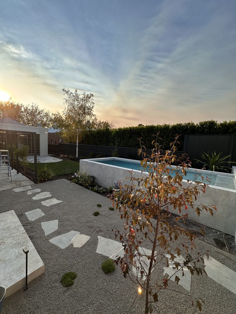 Raised plunge pool and stone stepping path in a landscaped backyard at sunset