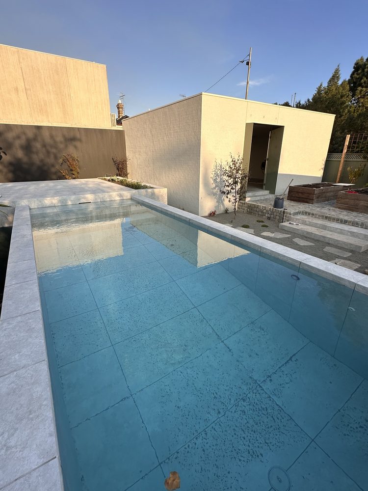 Newly built in-ground pool with stone coping and rendered feature walls