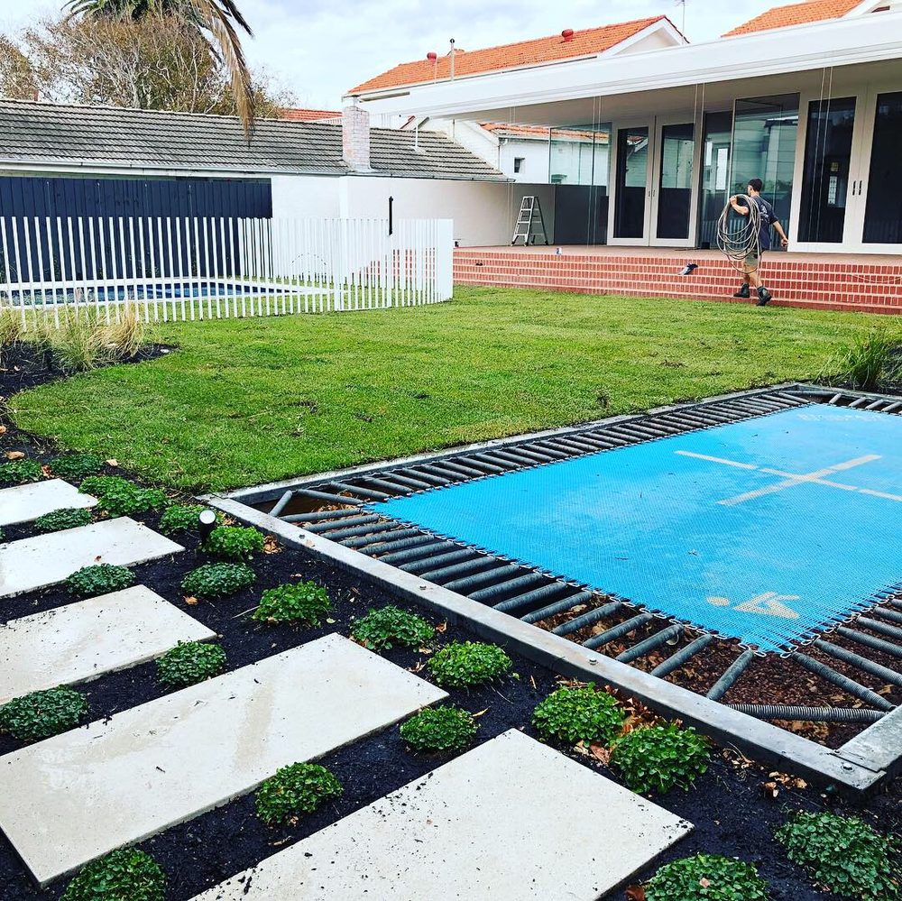 Backyard landscaping with new turf, an in-ground trampoline and sandstone stepping-stone path