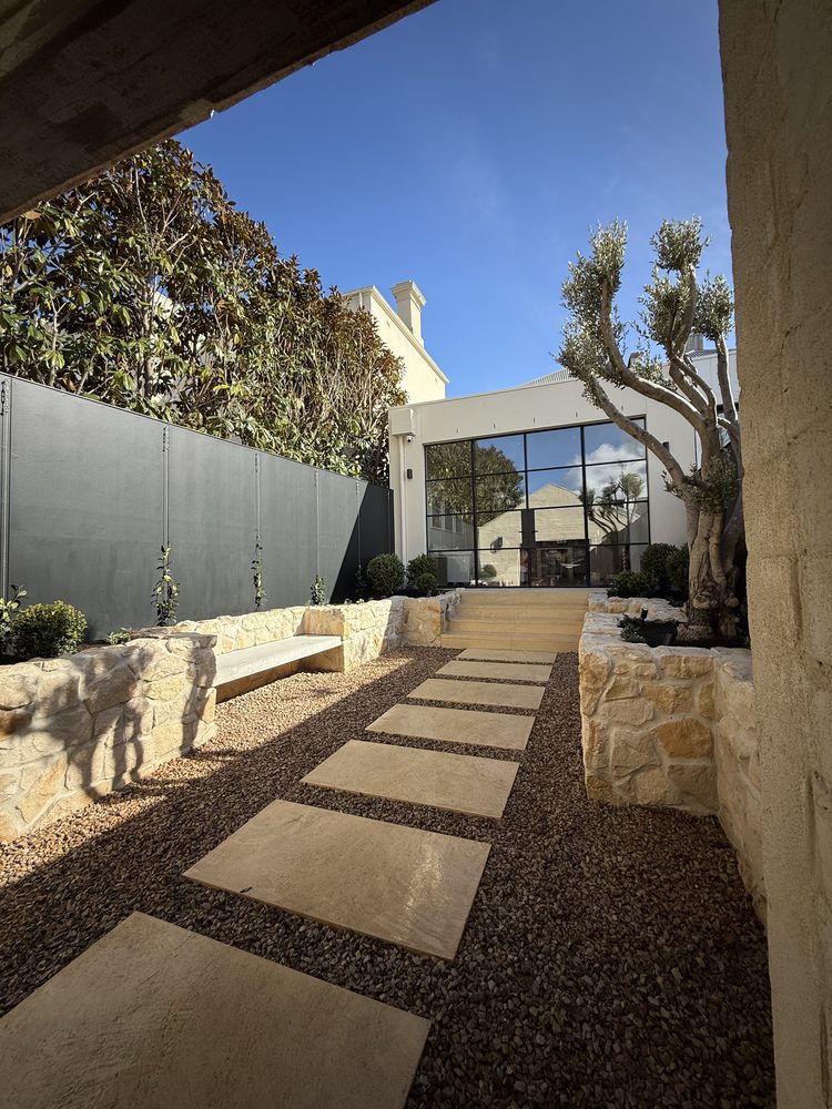 Landscaped courtyard with sandstone walls, a mature olive tree and a stone paver path