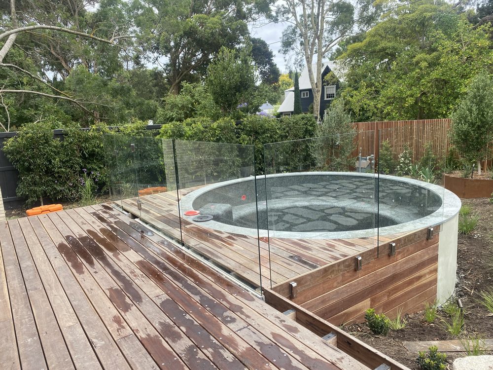 Frameless glass pool fence around a paved pool terrace with loungers