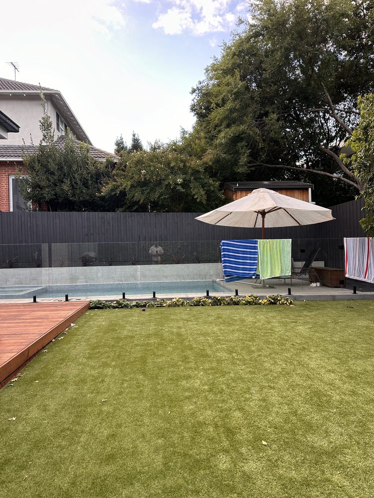 Curved black batten aluminium pool fence around a backyard pool with artificial lawn