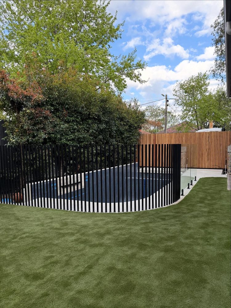 Curved black vertical-bar pool fence around a tiled pool with a water feature