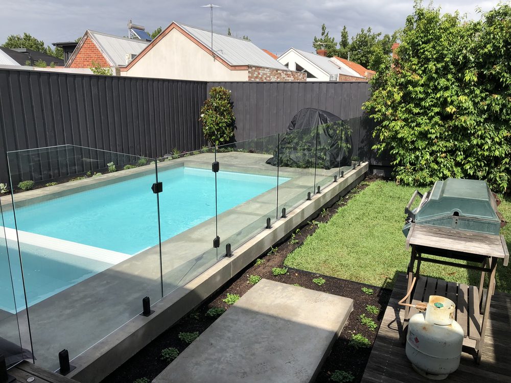 Frameless glass pool fencing on a concrete surround around a tiled backyard pool