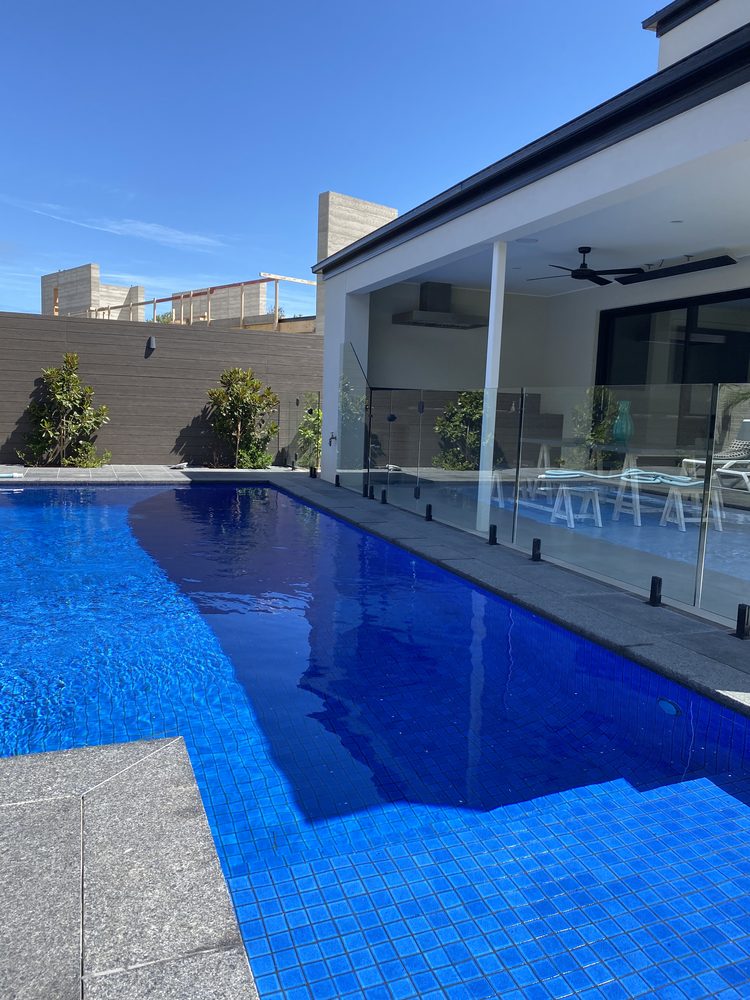Frameless glass pool fence being installed around a pool on a timber deck