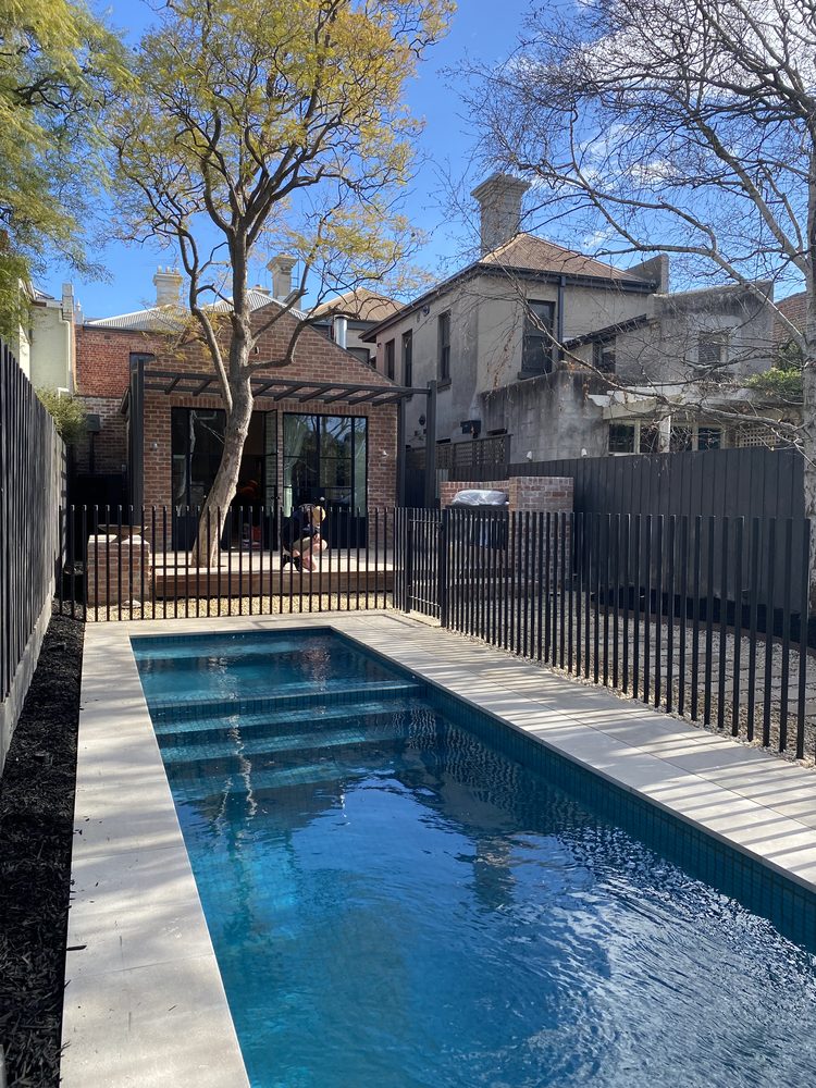 Black blade-style aluminium pool fence alongside a tiled lap pool